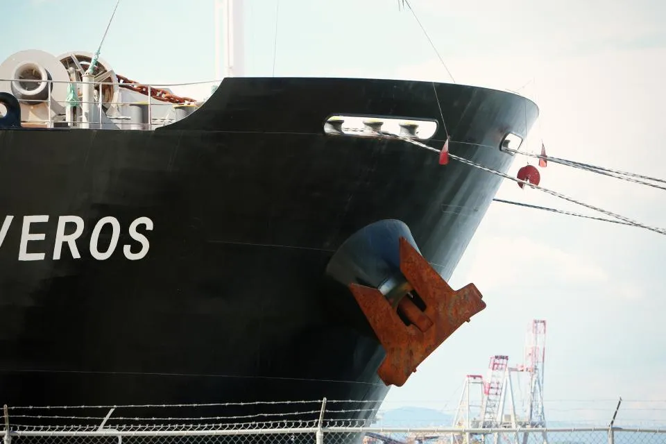 Bow of a black merchant ship with its anchor stowed and mooring lines out